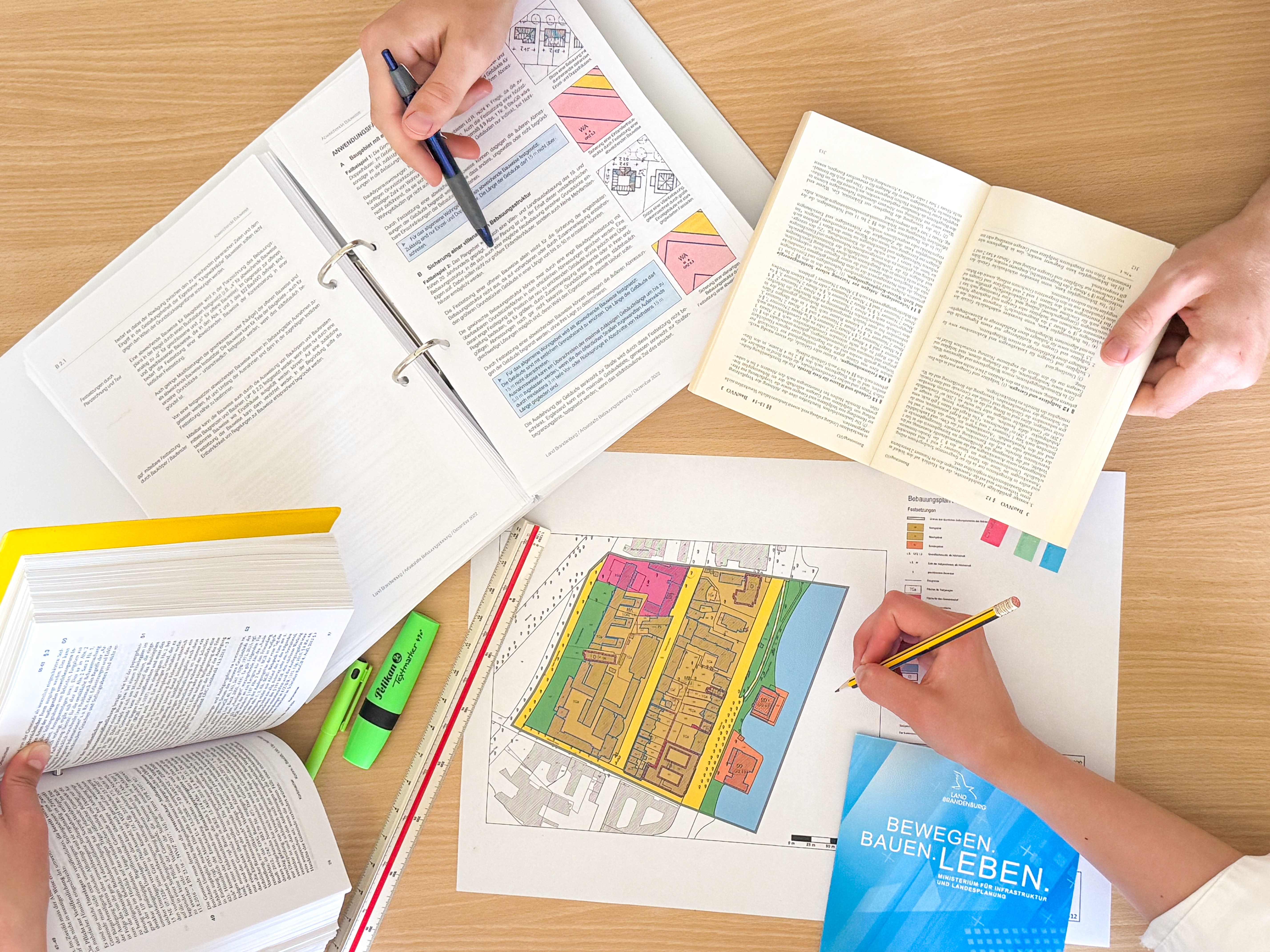Bauassessor Städtebau Mehrere Gesetzesbücher und Vorschriften sowie ein Bebauungsplan liegen offen auf einem Tisch.